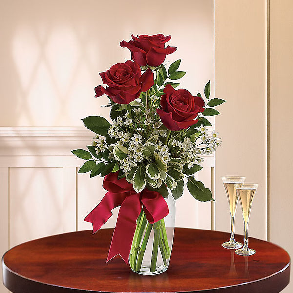 Bouquet of red roses with a red bow in a clear vase on a wooden table