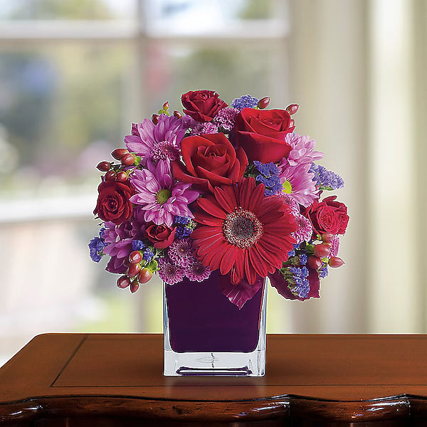 Vibrant flowers arranged in a glass vase with a soft background.