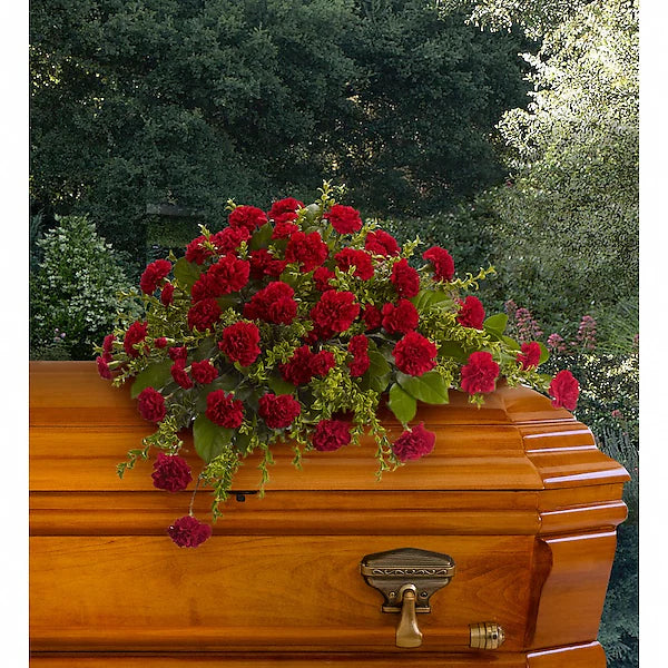 Wooden casket topped with decorative red blooms in natural backdrop