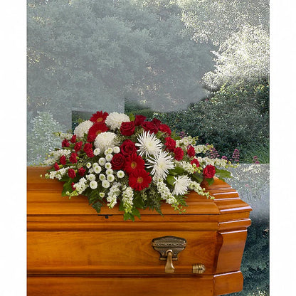 Vibrant red, white, and green floral arrangement on wooden casket outdoors