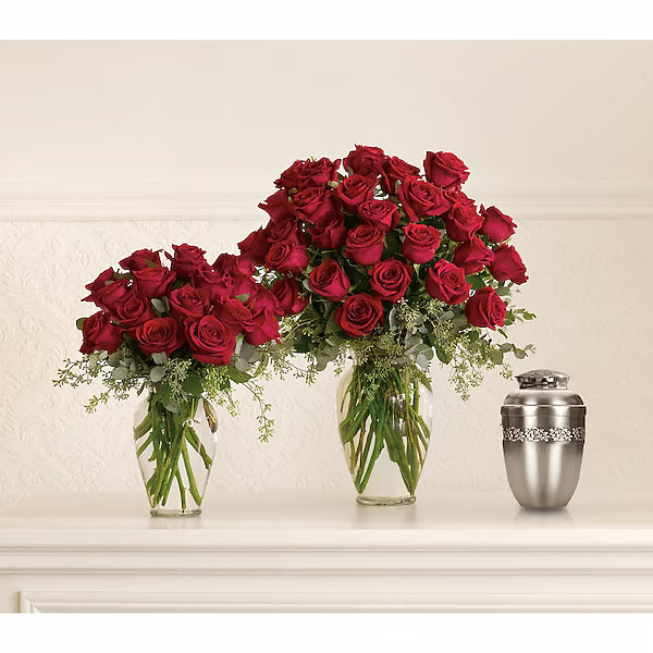 Red rose arrangements in glass vases beside silver urn