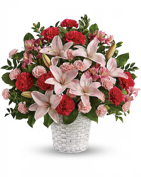 Bouquet of pink lilies and red carnations in a white woven basket on a white background