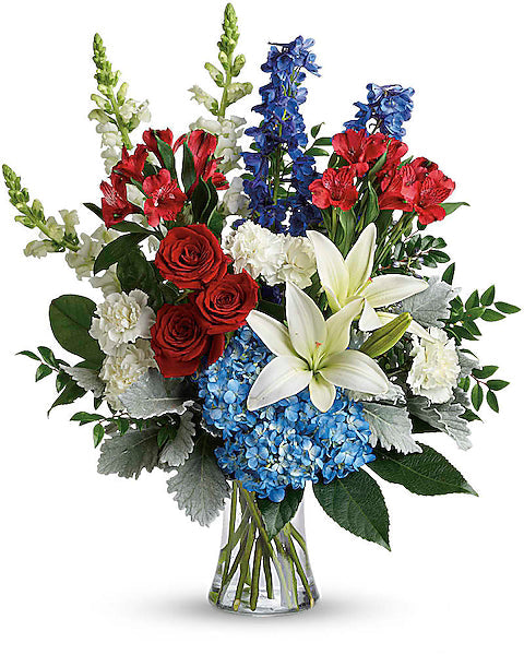 Bouquet of red, white, and blue flowers in a clear vase on a white background