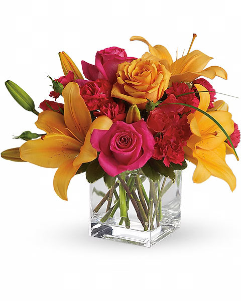 Colorful flower arrangement with yellow lilies and pink roses in a clear glass vase on a white background