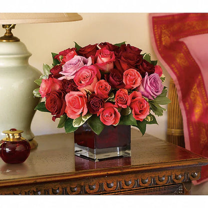 Bouquet of red, pink, and purple roses in a clear vase on a decorative table.