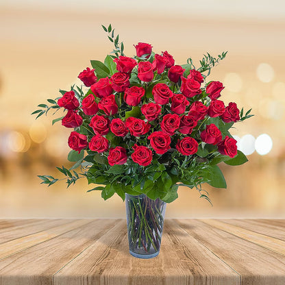 Bouquet of red roses in a clear vase on a wooden table with a blurred background